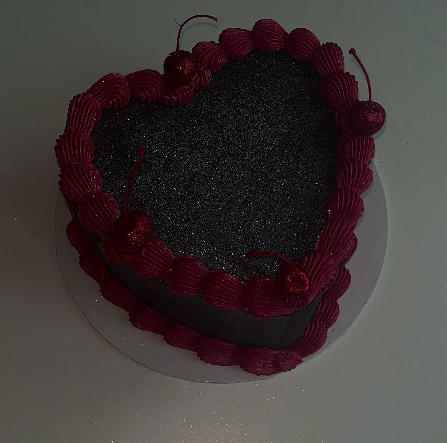 Black glitter heart cake edged with deep pink piping and glitter cherries